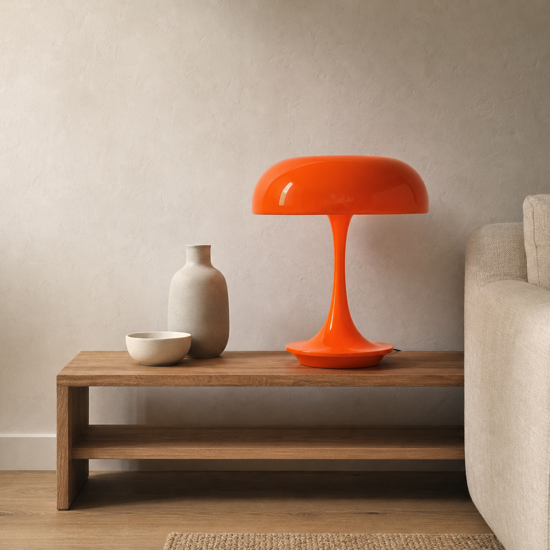 A bright orange mushroom-shaped table lamp sits on a wooden side table in a modern living room setting next to a beige sofa.