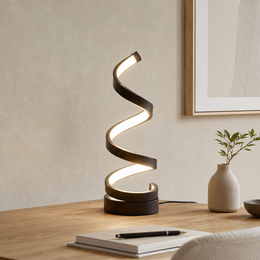 A modern spiral twist table lamp with a black base and illuminated white spiral arms, styled on a wooden desk next to a small vase with greenery.
