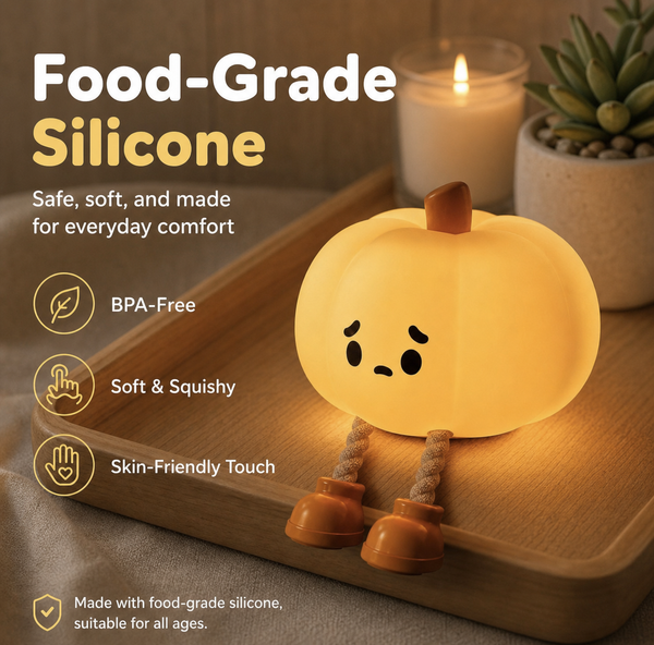 A glowing yellow-orange silicone pumpkin night light with a sad face and rope legs, placed on a wooden tray in a softly lit setting with a candle and succulent in the background. Text on the left highlights food-grade silicone, BPA-free, soft and squishy, and skin-friendly touch features.