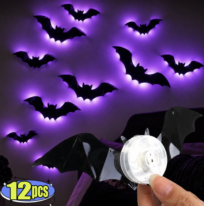 A set of 12 black bat-shaped LED night lights glowing with purple light on a dark wall, with a hand holding a battery pack in the foreground and a '12pcs' badge in the bottom left corner.