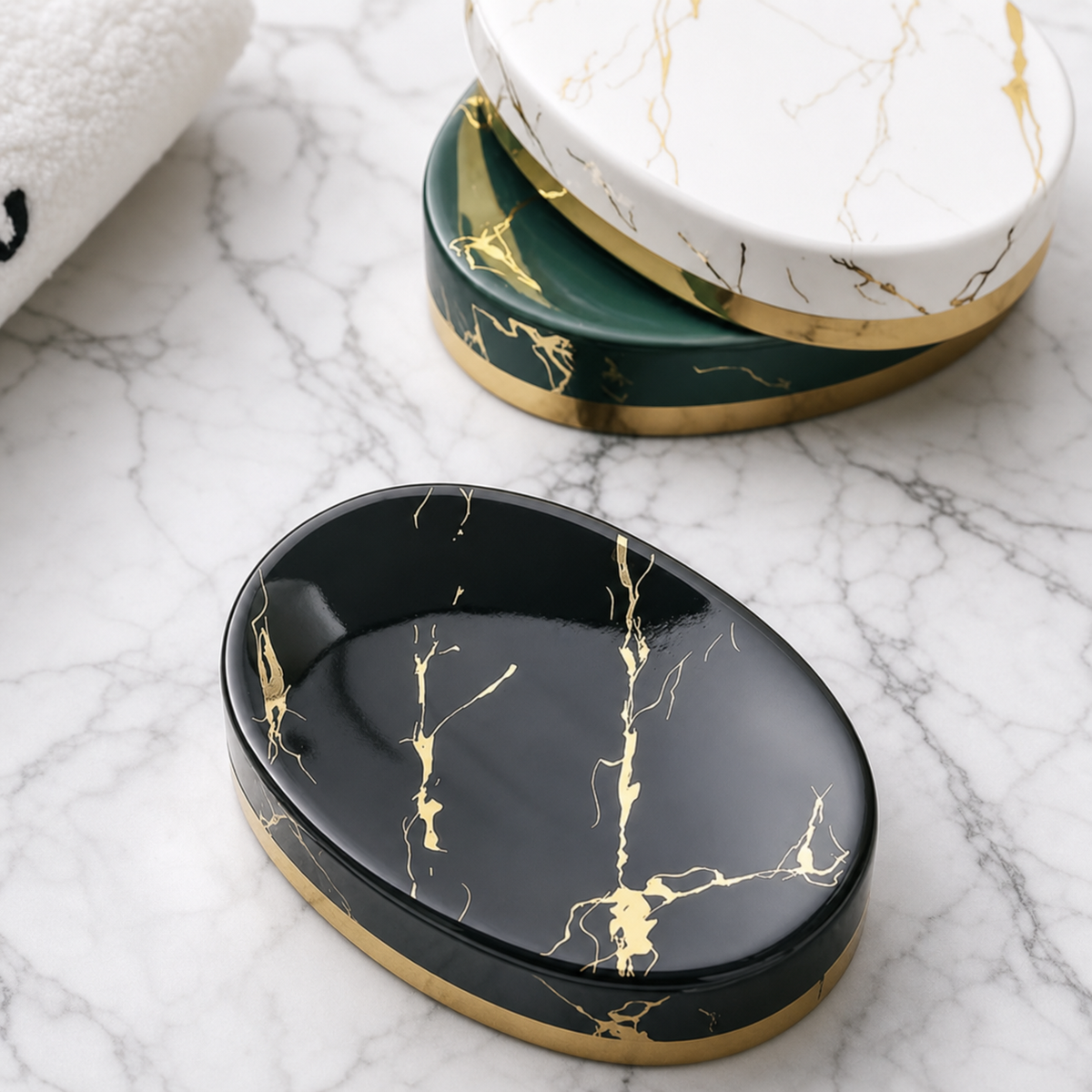 An oval black soap dish with a gold marble pattern and gold trim, shown on a white marble surface with two additional soap dishes stacked in the background.