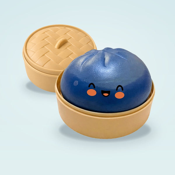 Dark blue squishy bun with a smiling face in a tan steamer basket, lid resting behind it