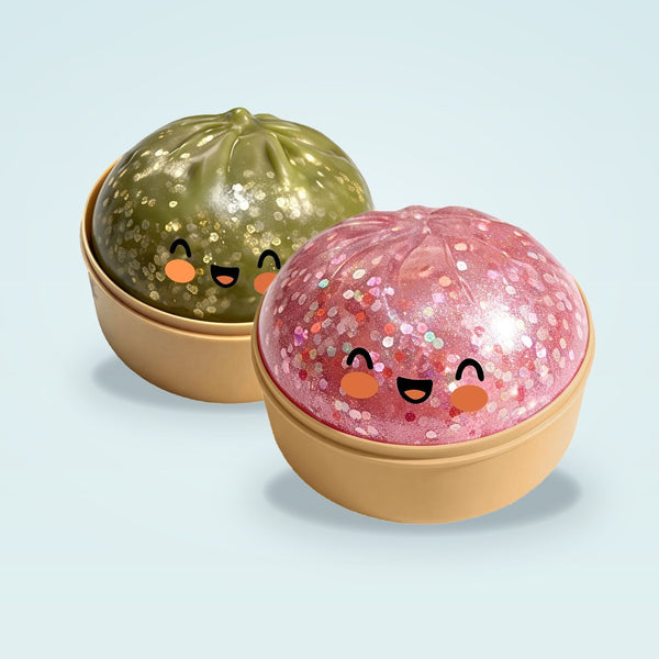 An olive green and a pink glitter squishy bun, each in its own tan steamer basket