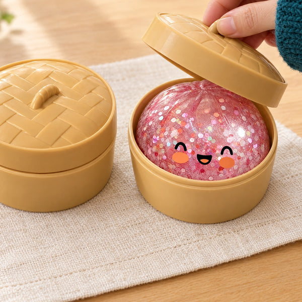 A hand lifts the lid of a steamer basket to show a pink glitter squishy bun, a second basket closed beside it (styled illustration)