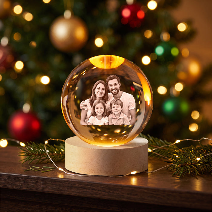 Personalized crystal ball night light glowing warm on a wooden shelf, a smiling family of four engraved inside the glass, Christmas tree lights blurred behind