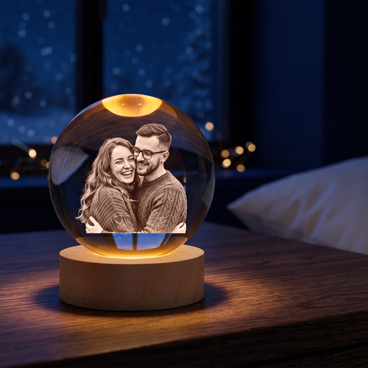 Crystal ball night light glowing warm on a nightstand at night, a laughing couple engraved inside, snowy window behind