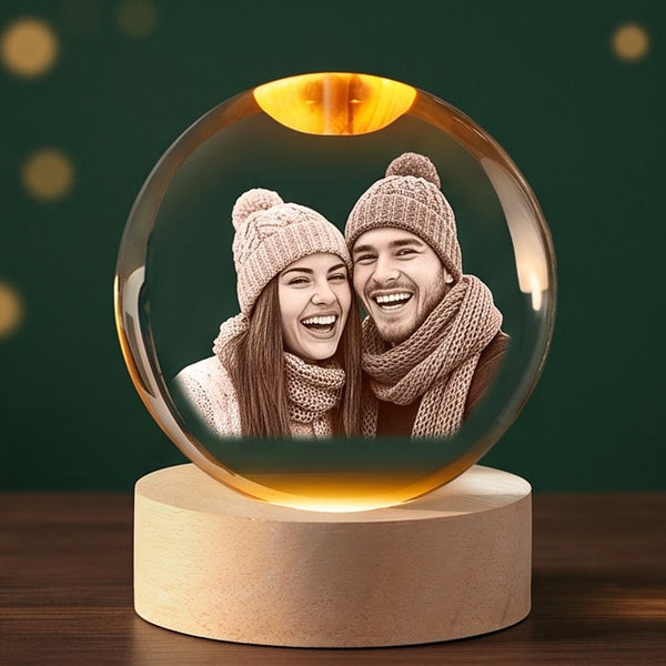 Example engraving: a laughing young couple in winter hats inside a glowing crystal ball on its wooden base.