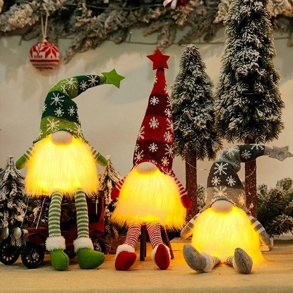 Three Long Legs gnomes glowing warm on a table with mini Christmas trees