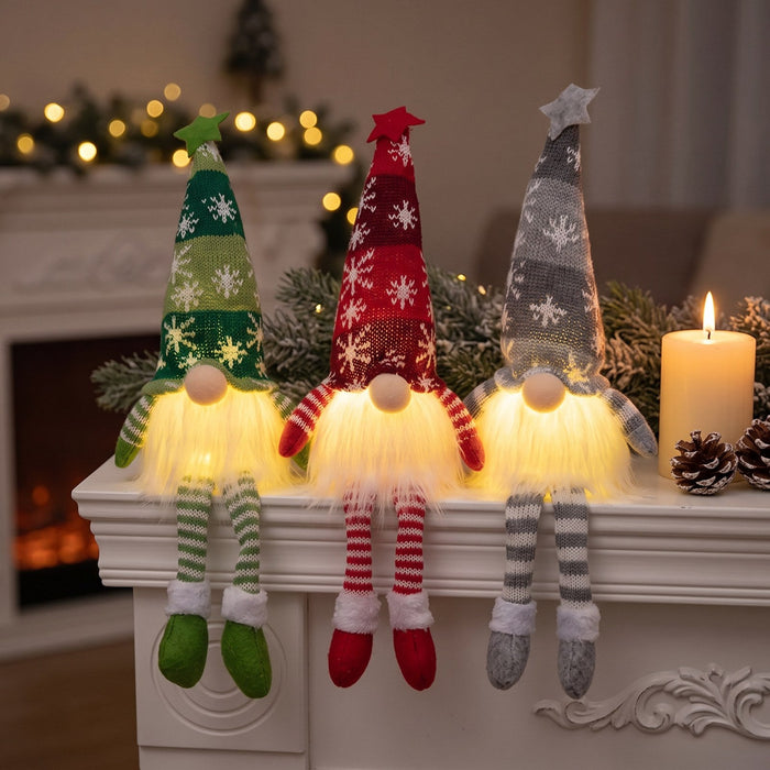 Three Long Legs Christmas gnomes in green, red and grey glowing on a white fireplace mantel beside a pillar candle