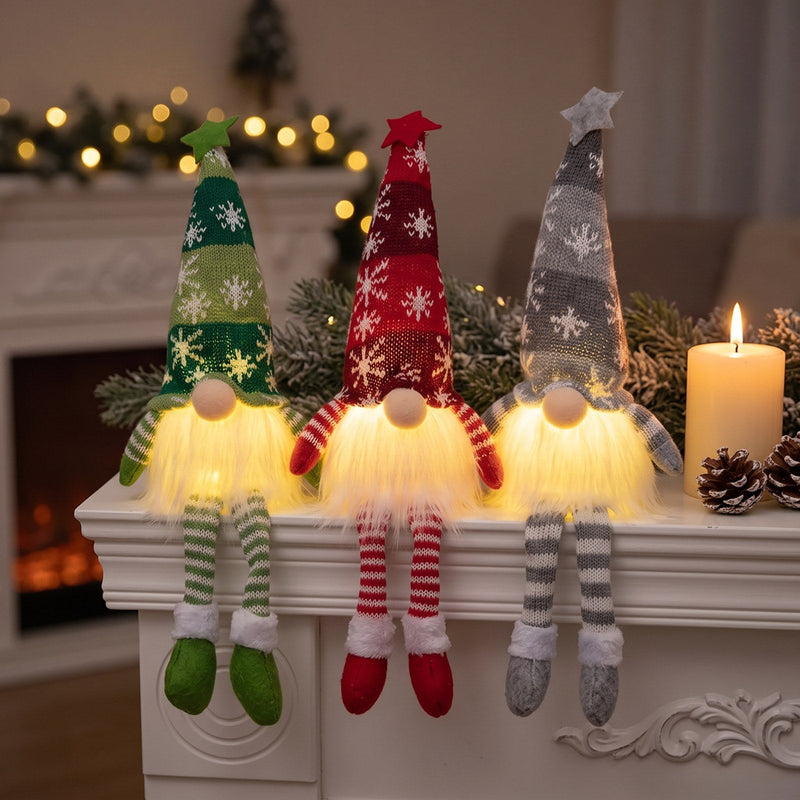 Three Long Legs Christmas gnomes in green, red and grey glowing on a white fireplace mantel beside a pillar candle