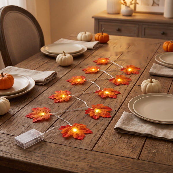 Styled scene: one strand with 10 glowing leaves down a wooden dinner table; tableware and pumpkins not included