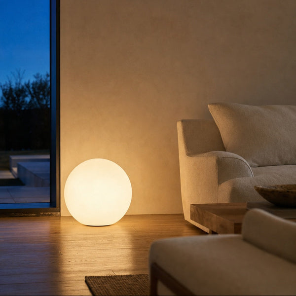 Glowing ball lamp on the floor beside a sofa at dusk